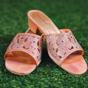 Stylish pink slip-on sandals with intricate designs placed on lush green grass, showcasing fashion elegance.